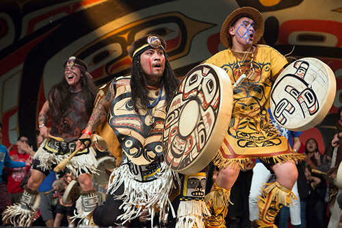 Git Hoan dancers wearing traditional regalia, perform tribal dances on stage.