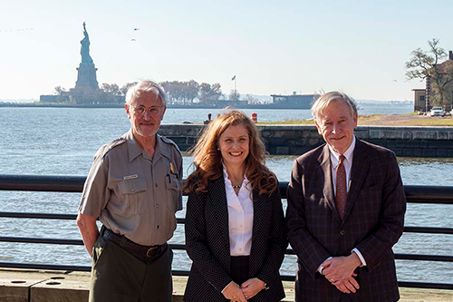 Three people standing with Statue of Liberty in background.