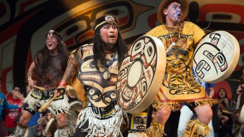 Git Hoan dancers wearing traditional regalia, perform tribal dances on stage.