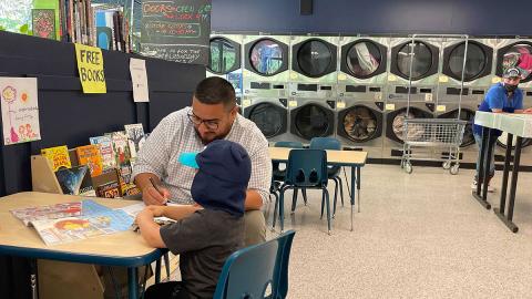 Wash and Learn library participants engage in table activity, and a row of coin laundry machines in the background.