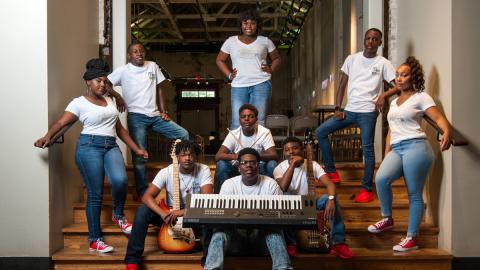 A group of gifted and talented teenagers, dressed in blue jeans and white shirts, pose with musical instruments on stage at the The B.B. King Museum and Delta Interpretive Center. 