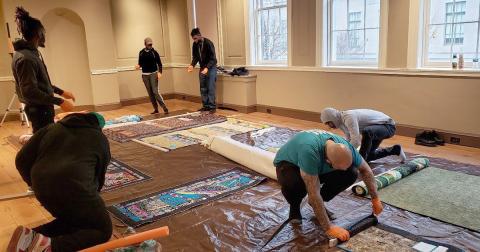 A group of people working on a rug in a room